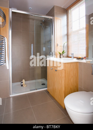 Portes en verre sur une grande douche à l'italienne dans une salle de bains moderne avec du carrelage beige et bois à lattes blind Banque D'Images