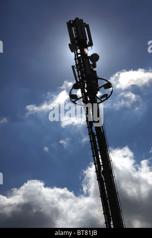 Mât de téléphonie mobile silhouetté contre le ciel bleu et les nuages. Banque D'Images