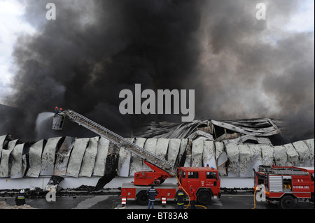 Camion pompiers sur une échelle à la lutte contre un incendie d'usine massive au milieu d'une épaisse fumée Banque D'Images