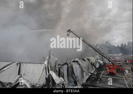 Les pompiers sur une échelle à coulisse la lutte contre un incendie d'usine massive au milieu d'une épaisse fumée Banque D'Images