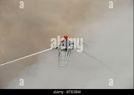 Les pompiers sur une échelle à coulisse la lutte contre un incendie d'usine au milieu d'une épaisse fumée Banque D'Images