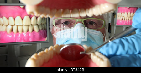 Un dentiste travaillant sur des modèles de dents avec tv affiche d'teeeth dans l'arrière-plan Banque D'Images