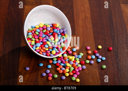 Fèves chocolat colorés en blanc bol sur table en bois Banque D'Images
