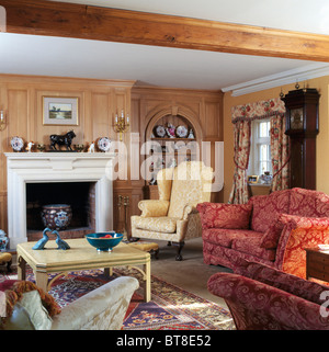 Aile crème-chaise et canapé rouge à motifs en pays lambrissés salon avec crème peint table en face d'une cheminée Banque D'Images