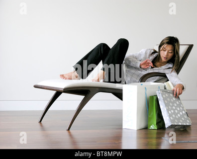Jeune femme sur une chaise longue d'ouvrir les sacs de retour accueil Banque D'Images