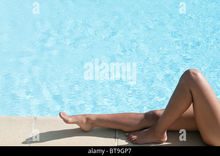 Les jambes d'une jeune femme bronzer au bord d'une piscine Banque D'Images