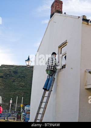 L'homme sur une échelle à la fenêtre d'une maison de nettoyage Staithes North Yorkshire Banque D'Images