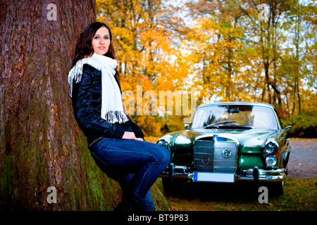 Jeune femme appuyée contre un arbre en face d'une voiture d'époque, MB 220 SE Cabriolet, construit en 1964 Banque D'Images