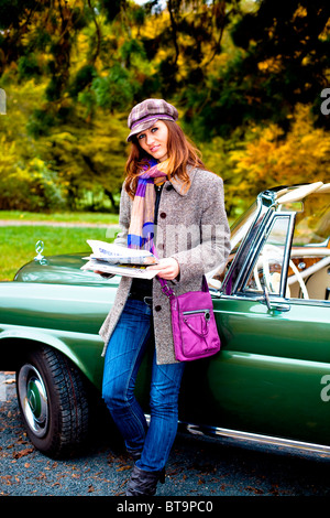 Jeune femme avec un journal appuyé contre une voiture d'époque, MB 220 SE Cabriolet, construit en 1964 Banque D'Images