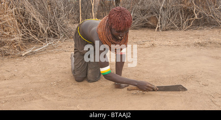 Les Nyangatom (Bumi) une femme sur ses genoux et gratter le sol avec une machette, vallée de la rivière Omo, en Ethiopie Banque D'Images