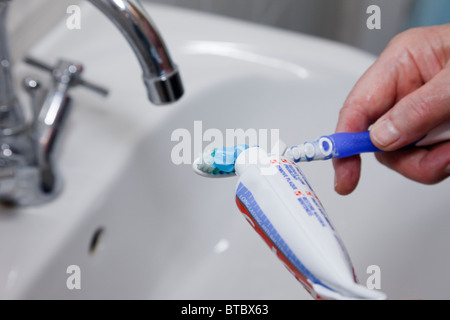 Close-up d'une personne qui met du dentifrice sur une brosse à dents à plus d'un lavabo. En Angleterre, Royaume-Uni, Grande Bretagne. Banque D'Images
