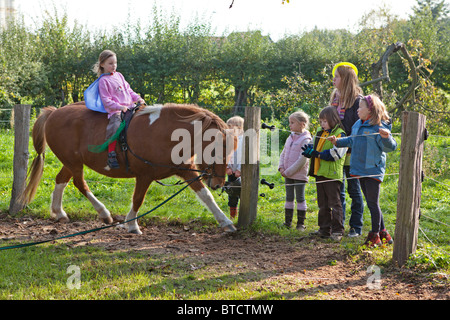 Little girl lying équitation un poney, d'autres filles la regarder Banque D'Images