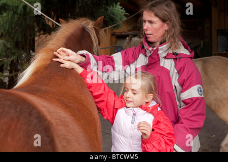 Petite fille de toucher un poney avec ses yeux fermés dirigée par son professeur d'équitation Banque D'Images