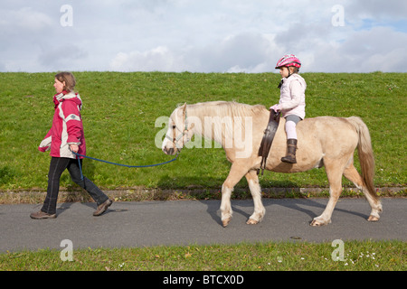 Petit Poney girl riding a dirigée par son professeur d'équitation Banque D'Images