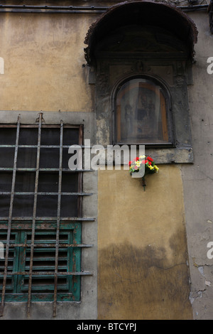 Couleurs vives de fleurs en plastique bouquet sous miteux et religieux en décomposition murale sur mur de Florence. Banque D'Images