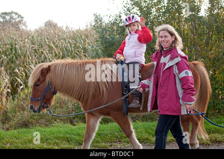 Petit Poney girl riding a dirigée par son professeur d'équitation Banque D'Images