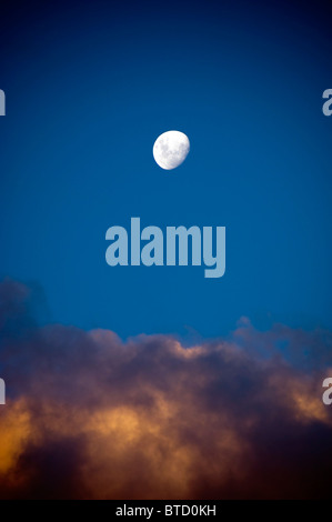 Presque pleine lune blanc brillant se lève sur dernière lumière dans les nuages Banque D'Images