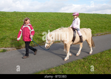 Petit Poney girl riding a dirigée par son professeur d'équitation Banque D'Images