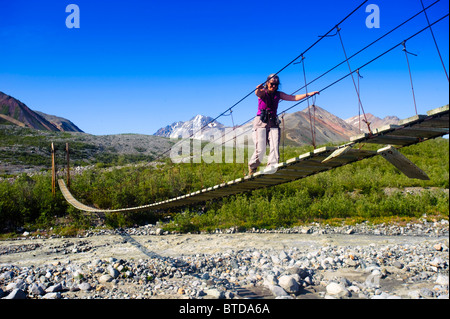 Une femme marche sur un pont suspendu au College Creek à Gulkana, Southcentral Alaska Glacier Banque D'Images