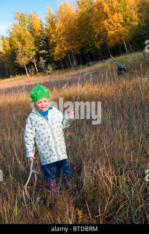 Female toddler portant un chapeau vert joue avec des bâtons de bois flotté sur les vasières à côté du sentier du Littoral, Anchorage, Alaska Banque D'Images