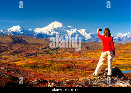 Une femme de la randonnée dans les collines de Peters s'arrête pour prendre une photo de Mt. McKinley avec son téléphone cellulaire, Denali National Park, Alaska Banque D'Images