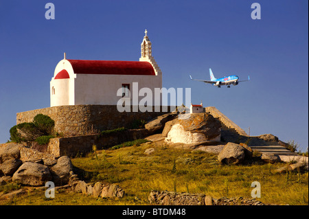 L'un des centaines de chapelles traditionnelles au toit rouge sur Mykonos, avec un avion à l'atterrissage, Islads Cyclades, Grèce Banque D'Images