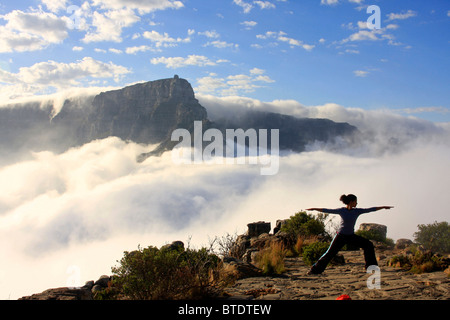 Une femme tenant un yoga pose sur le dessus de la tête des Lions avec un avis de la banque ci-dessous les nuages et la montagne de la table en arrière-plan Banque D'Images