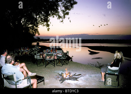 Les clients de Tafika camp assis autour d'un feu de camp avec vue sur la Rivière Luangwa au crépuscule Banque D'Images