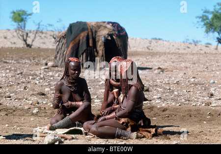 Trois femmes Himba adultes habillés en vêtements traditionnels assis dans un demi-cercle en face de leur bâton et la peau d'animaux accueil Banque D'Images