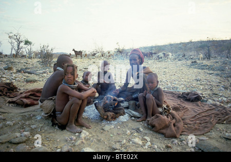 L'homme et des enfants Himba assis autour d'un feu avec les chèvres dans l'arrière-plan Banque D'Images