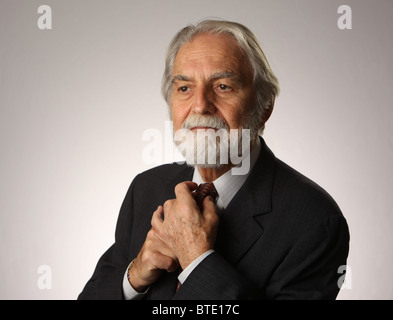 Portrait de phoque barbu et aux cheveux gris senior businessman ajustant sa cravate, studio shot, blanc, fond gris, 16 Octobre 2010 Banque D'Images