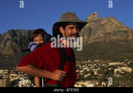 Un homme barbu portant un chapeau randonnées avec son fils dans un transporteur à Camps Bay, la Montagne de la table (Modèle 1992) Banque D'Images