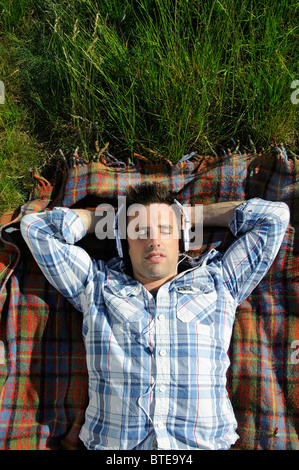 Young man lying on blanket et listening to headphones outdoors Banque D'Images