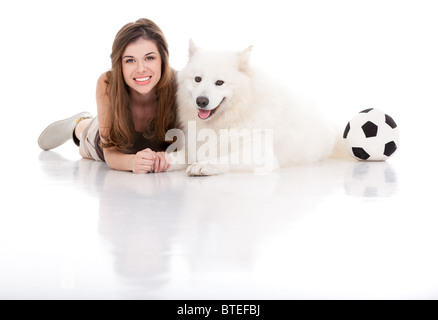 Un studio image d'une jeune femme avec un chien blanc, tous deux posant par assis leur ventre, tenant les mains, souriant, avec un ballon de football sur Banque D'Images