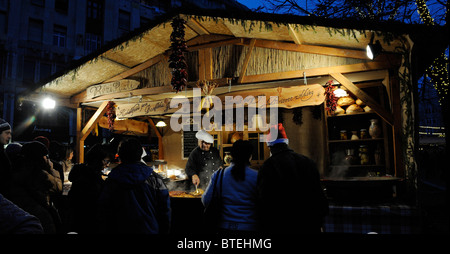 La foule se rassembler autour d'elle la petite stalles en bois traditionnelle de vente au marché de Noël de la place Vorosmarty, Budapest, Hongrie Banque D'Images