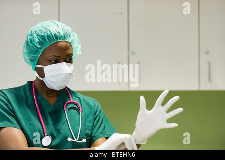 Nurse wearing surgical mask putting on latex gloves Banque D'Images