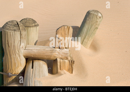 Vieille clôture en bois poteaux à moitié enfoui dans le sable de la plage Banque D'Images