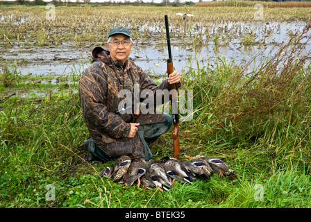 Heureux, wet Asian Canadian chasseur de canard à côté d'un champ inondé holding Benelli fusil de chargement avec une limite de canard colvert Banque D'Images