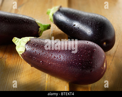 Les aubergines fraîches entières ou d'aubergines avec de l'eau gouttelettes, uncut et ONU-cuit contre un arrière-plan bois Banque D'Images