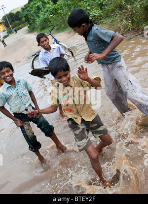 Les enfants indiens de sauter et de s'éclabousser dans l'eau sur une route inondée dans l'Andhra Pradesh, Inde Banque D'Images