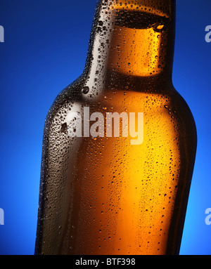 Bouteille de bière avec des gouttes sur un fond bleu. Fermer une partie de la bouteille. Banque D'Images