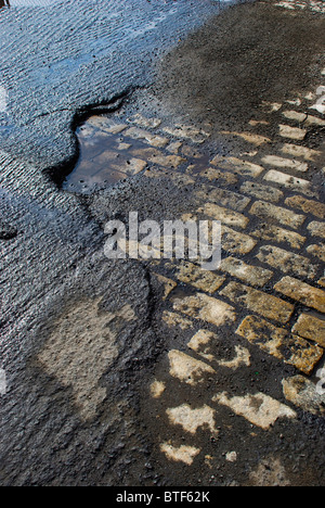 La fondation en pierre apparente sous route macadam malmenés après un resurfaçage attend la pluie. Banque D'Images