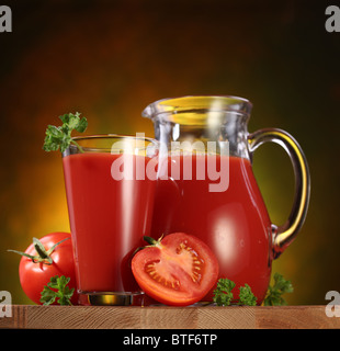 Still Life : tomates, verseuse en verre et plein de jus de tomates fraîches sur la table en bois. Banque D'Images