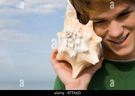 Jeune homme à l'écoute de coquille de conque Banque D'Images