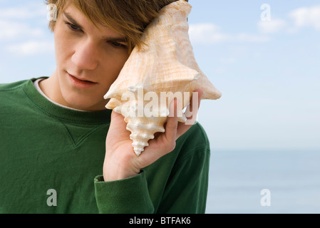 Jeune homme à l'écoute de coquille de conque Banque D'Images