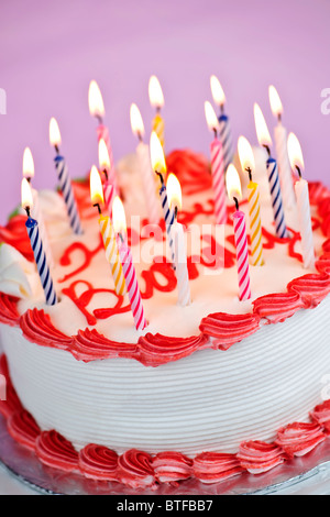 Gâteau d'anniversaire avec des bougies allumées et cerise sur fond rose Banque D'Images