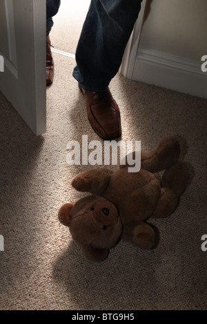 Ours en peluche de l'enfant allongé sur le sol d'une chambre dotée de moquette que celui d'un homme pieds entrez dans une porte ouverte Banque D'Images