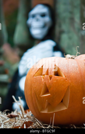 Une citrouille d'Halloween avec un visage sculpté assis sur une botte de paille avec un accent de squelette dans l'arrière-plan. Banque D'Images