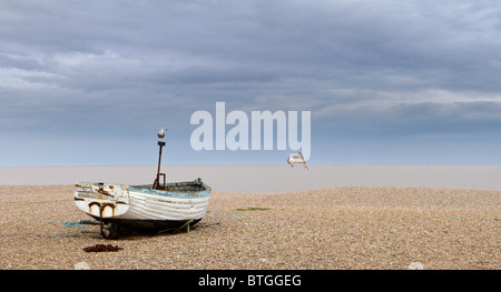 Un petit bateau de pêche sur la plage de galets à Aldeburgh, avec un ciel dramatique derrière et une mouette voler passé Banque D'Images