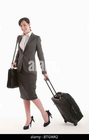 Jeune femme en costume avec valise à roulettes Banque D'Images